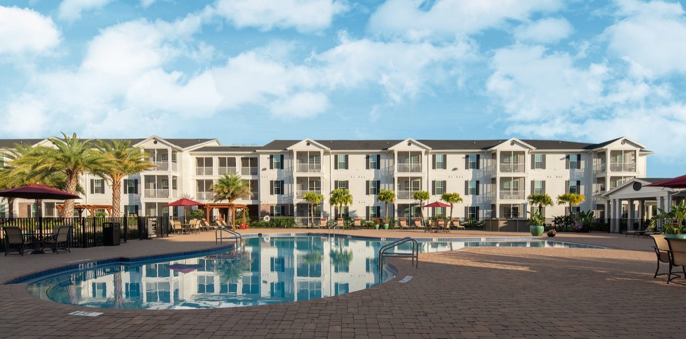 Outdoor resort-style pool with covered umbrella tables nearby and lounge seating