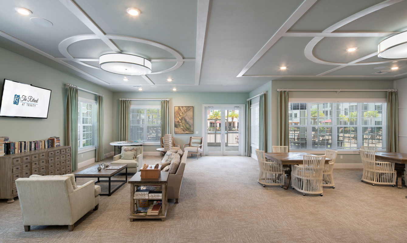 Interior of apartment clubhouse with card tables, TV, bookshelves, and comfortable seating