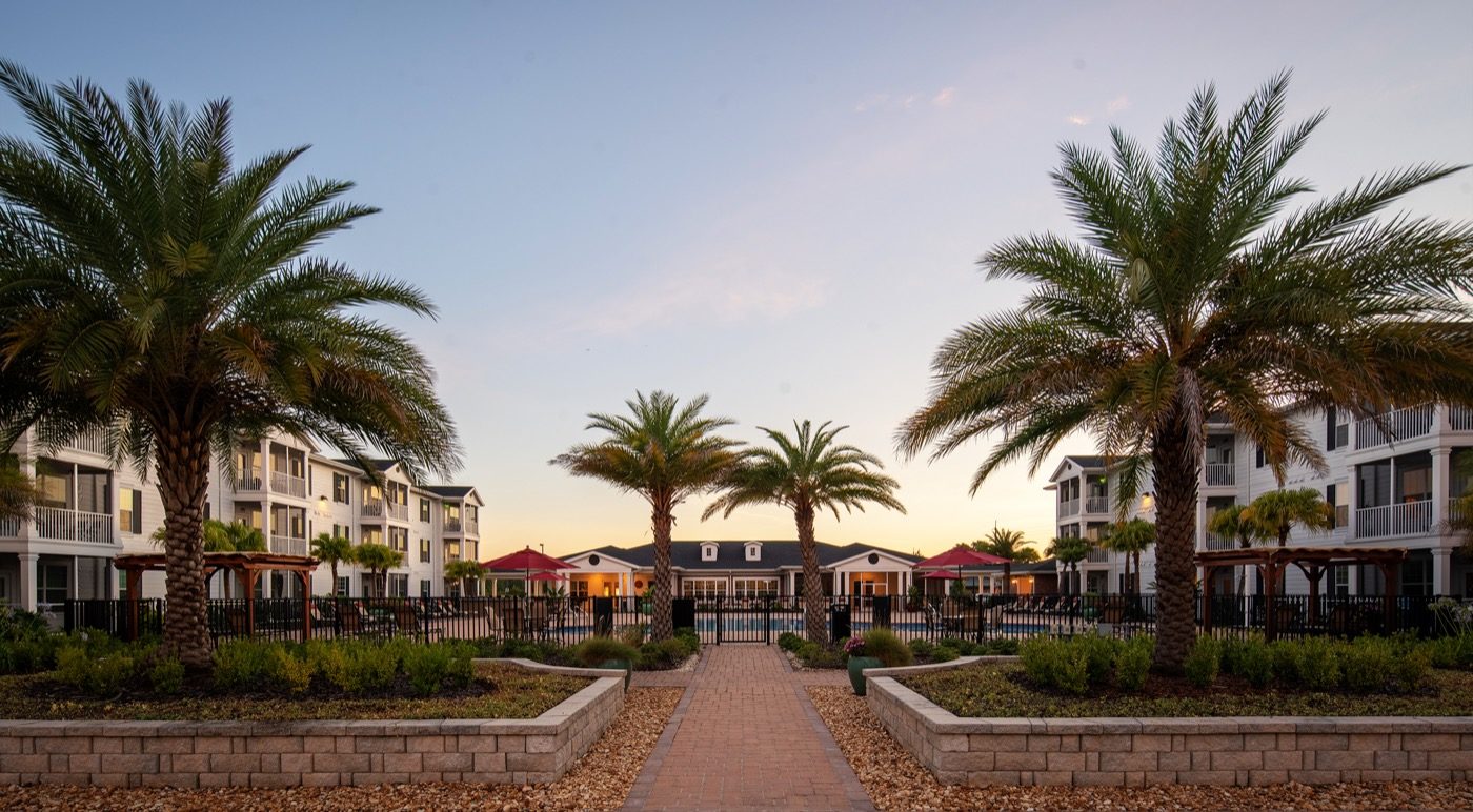 Sunset photograph of gated pool area with palm trees facing community clubhouse