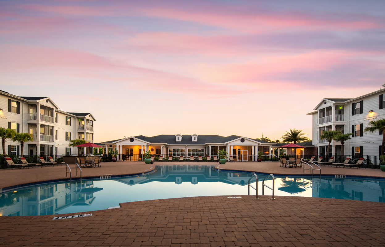 Sunset view of large resort-style swimming pool with gated enclosure