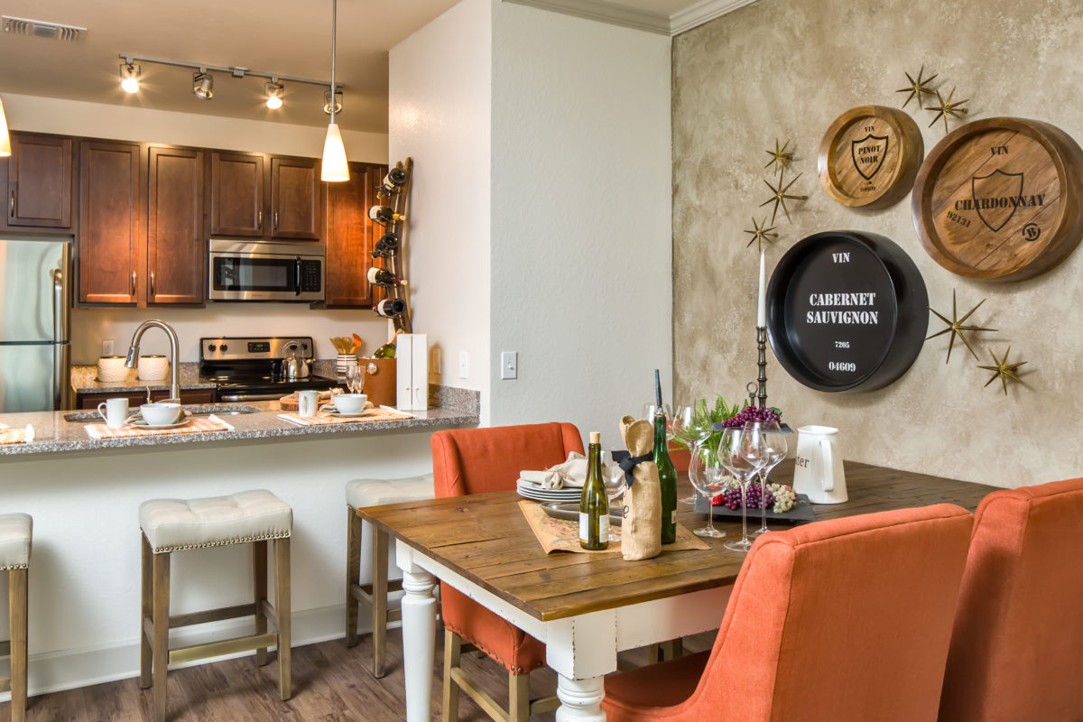 Model apartment kitchen and dining interior with espresso cabinets, stainless steel appliances, granite countertops, and bar seating