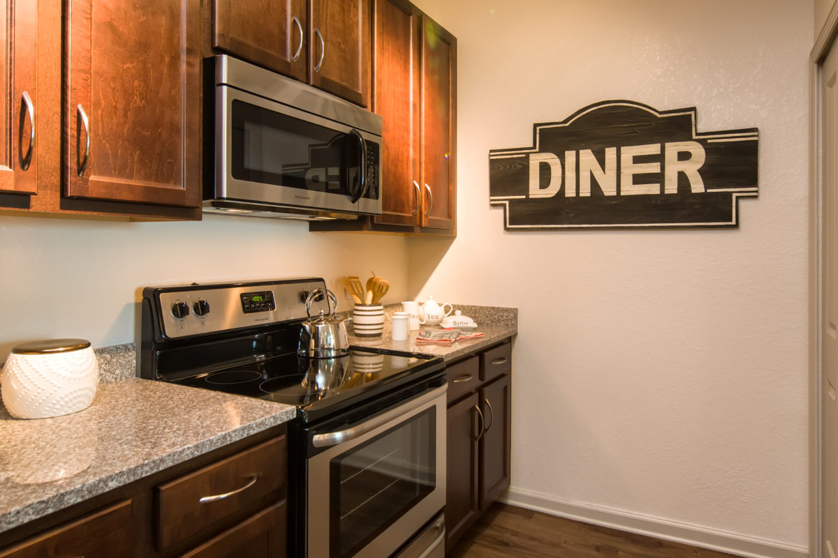 Alternate view of model apartment kitchen with granite countertops, espresso cabinets, and stainless steel appliances