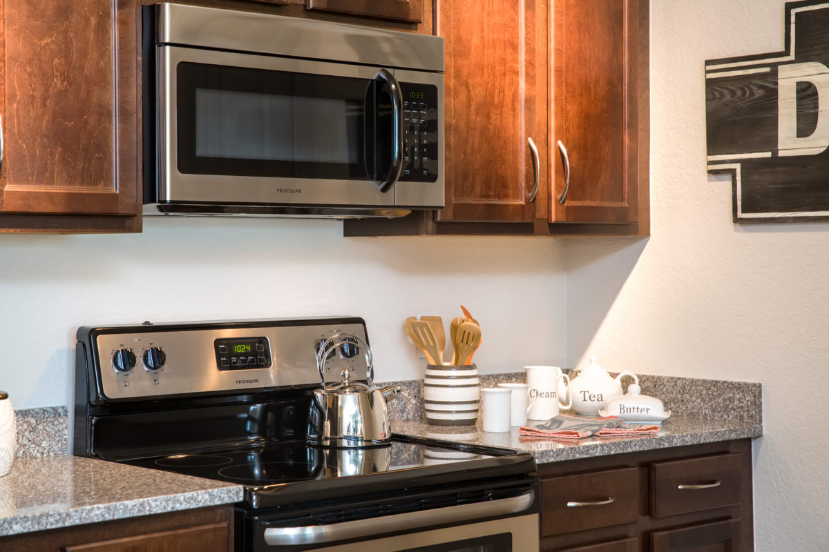 Close-up view of model apartment kitchen with stainless steel microwave and oven with granite countertops and espresso cabinets