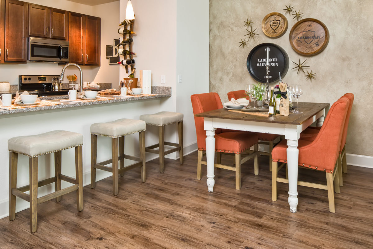 Model apartment dining area with hardwood flooring, barstools, and view of kitchen with espresso cabinets and granite countertops