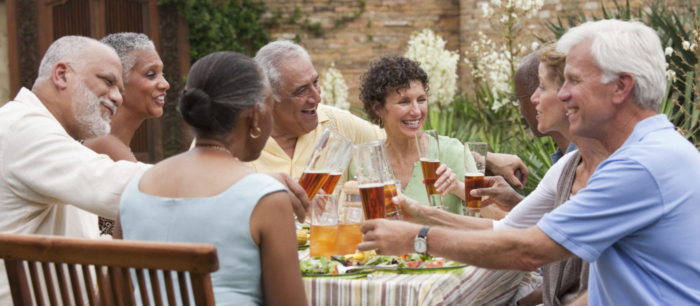 Group of happy senior friends seated around outdoor table toasting drinks