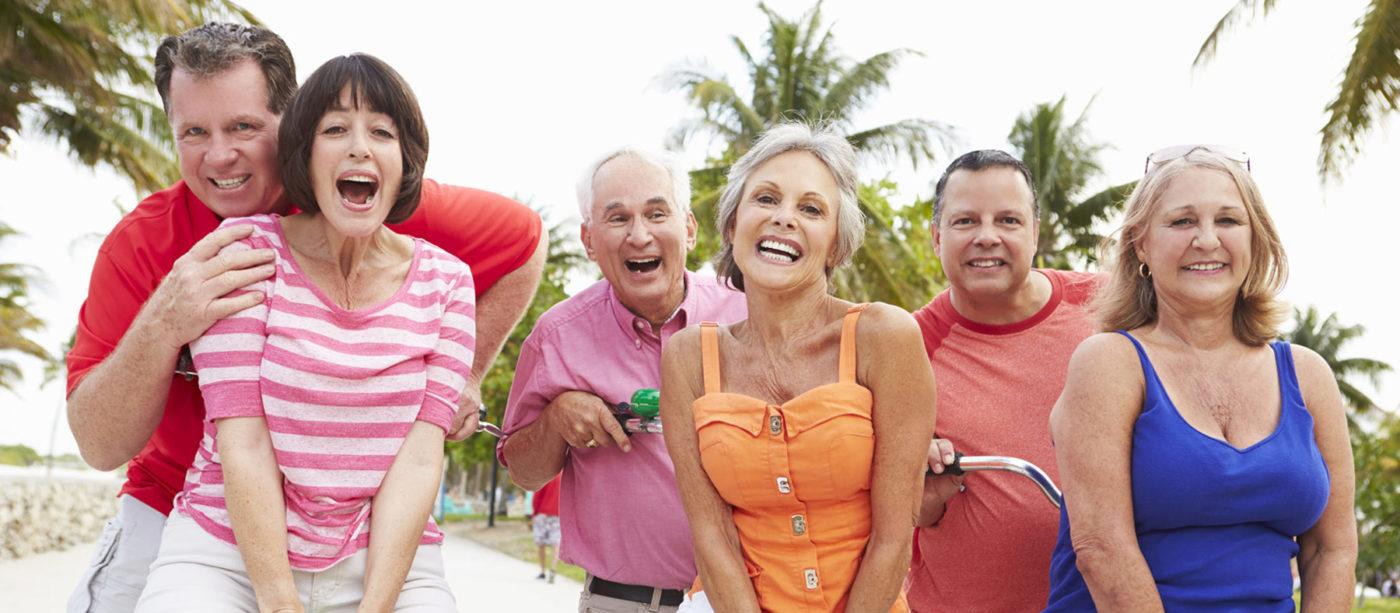 Happy senior friends smiling for camera near palm trees