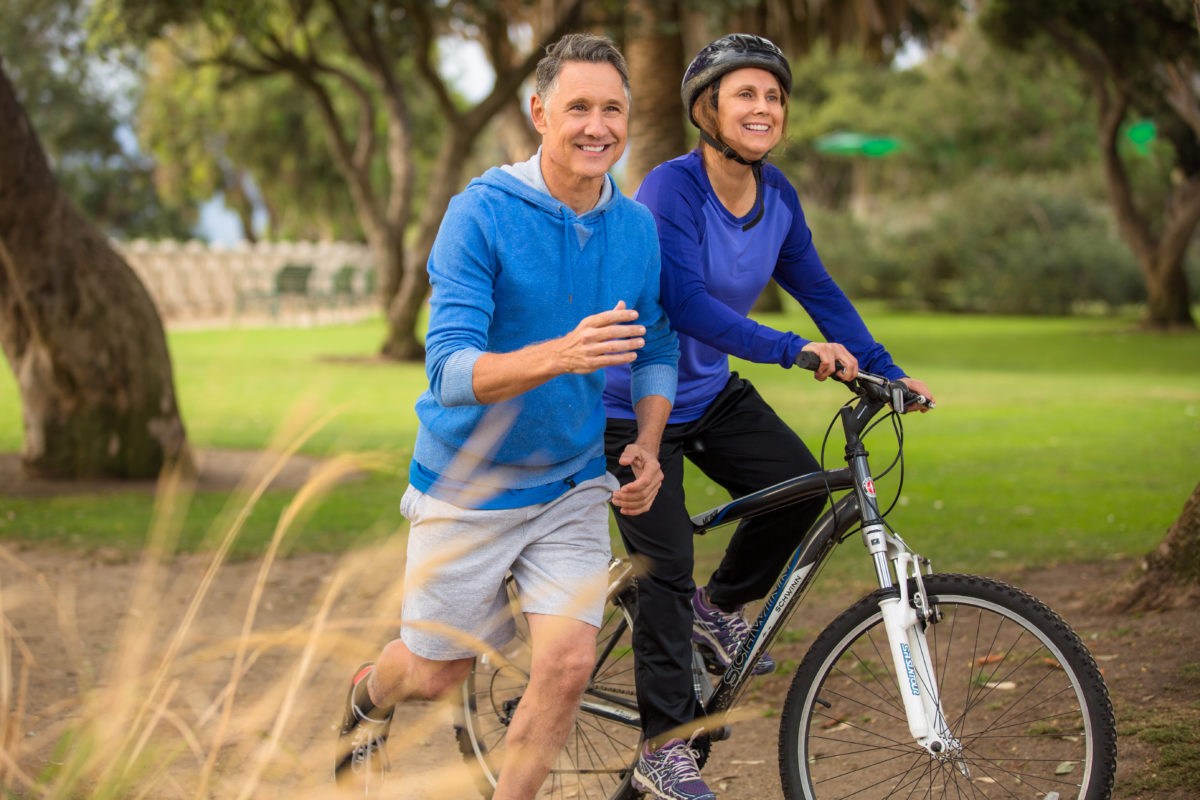 Happy senior couple jogging and riding bicycle outdoors